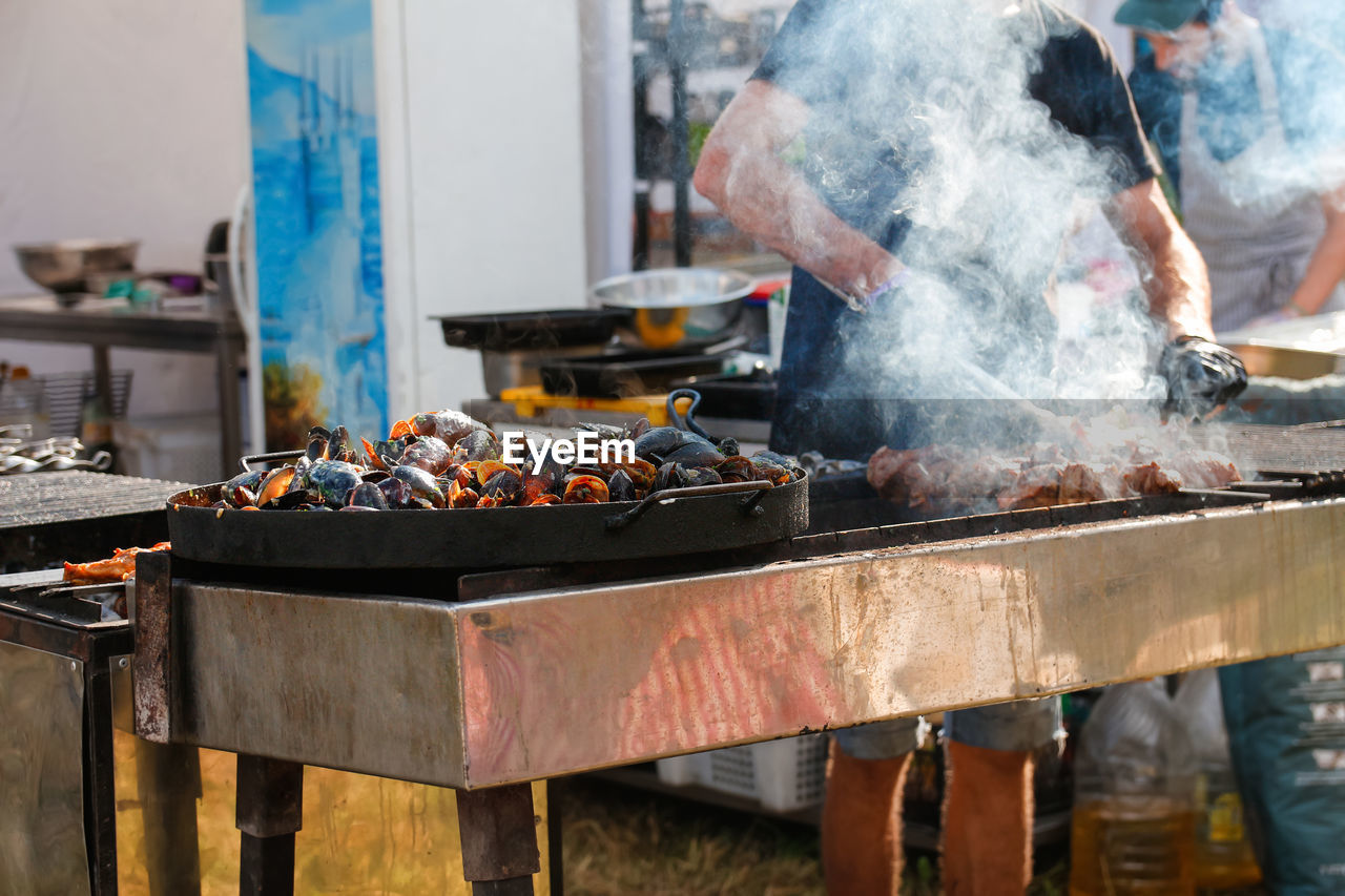 Man cooking bbq meat at festival outdoor. seafood paella. chef grilling sausages in park outside.