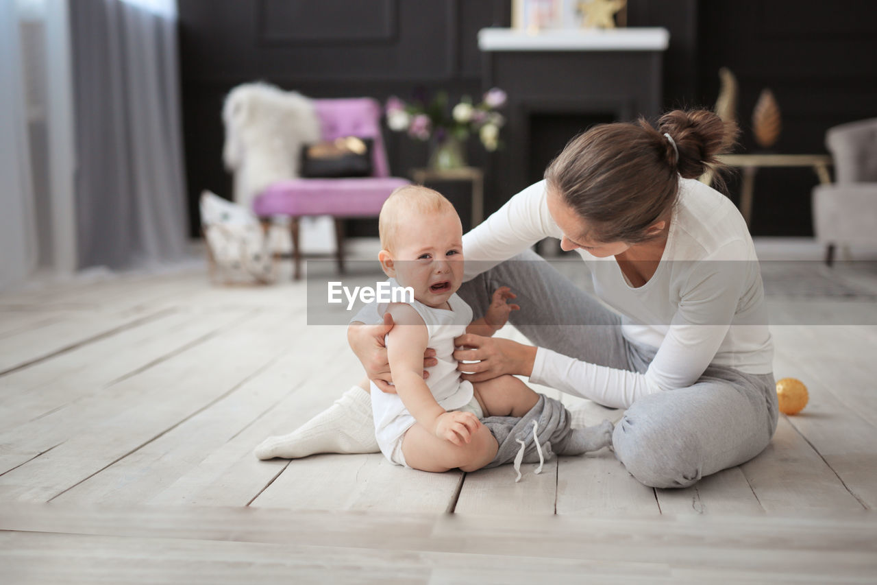 Mom and son are 11 months together on the floor, mom changes clothes for the baby, the boy cries.