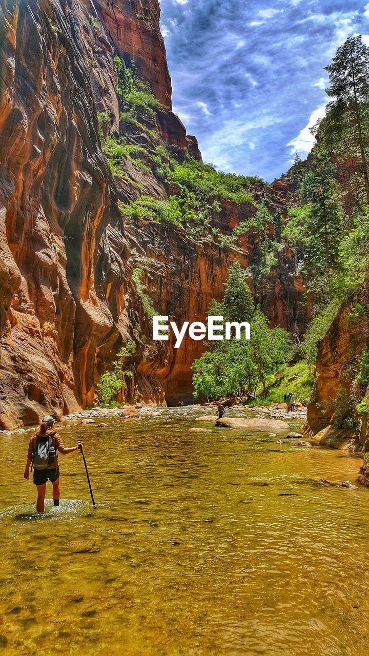 REAR VIEW OF MAN ON RIVERBANK AGAINST SKY