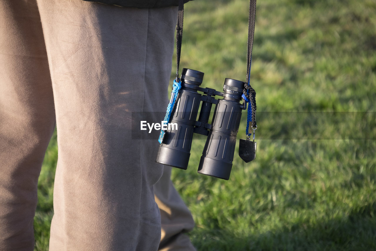 Midsection of person with binoculars standing on grassy field