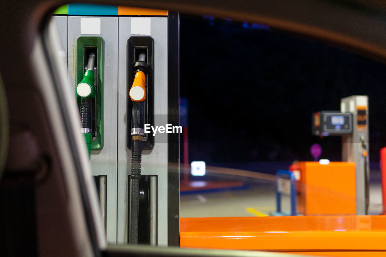 Through window of modern car of gasoline pumps with nozzles at filling station against dark night sky