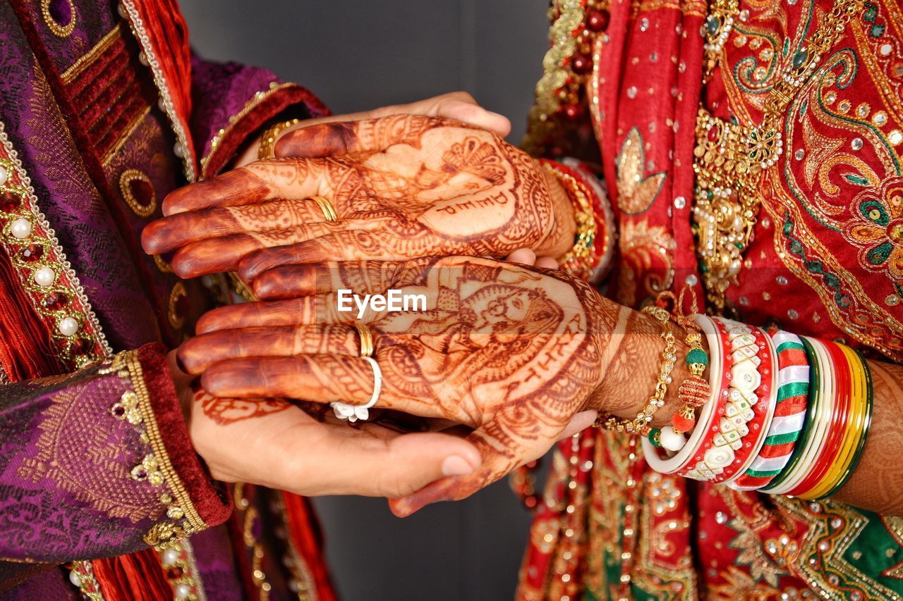 Midsection of groom holding bride hands with henna tattoo