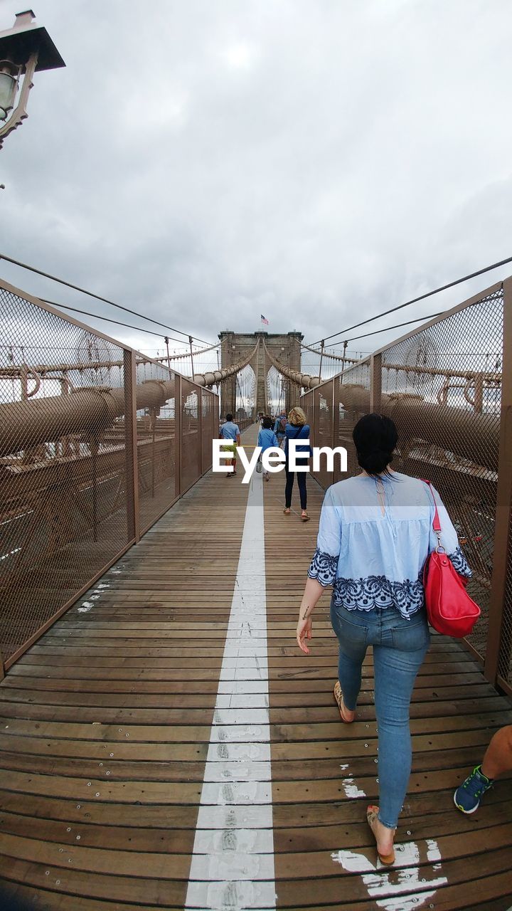 REAR VIEW OF PEOPLE IN FOOTBRIDGE AGAINST SKY