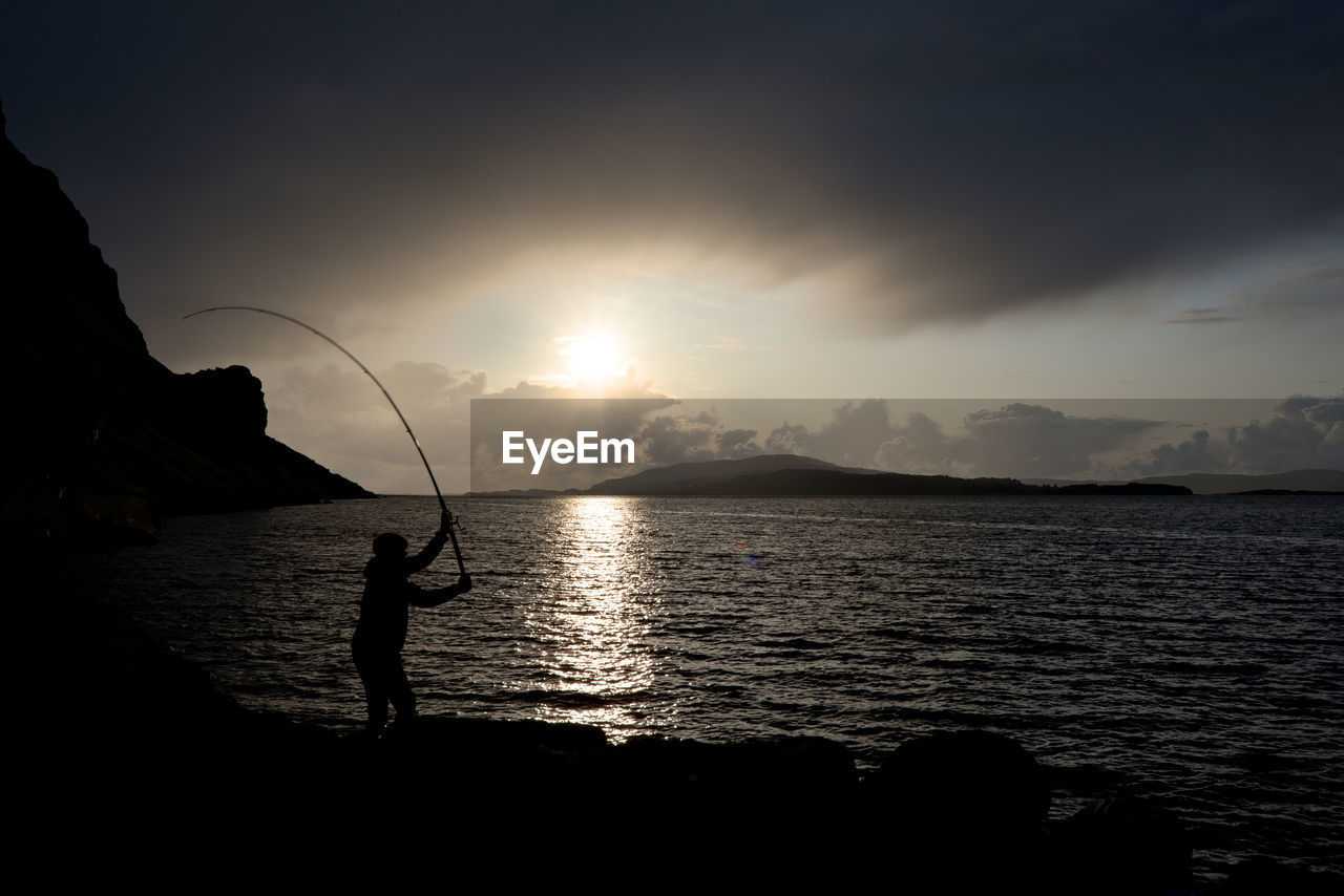 SILHOUETTE MAN FISHING IN SEA AGAINST SKY DURING SUNSET