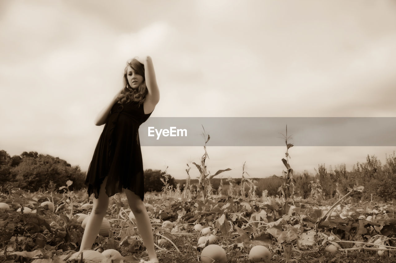 WOMAN STANDING ON FIELD AGAINST SKY IN BACKGROUND