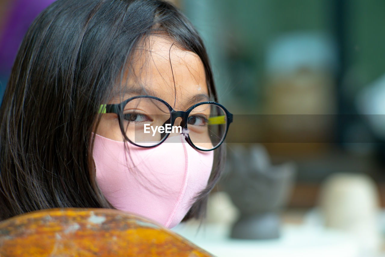 Closeup face of young girl wearing eyeglasses and facial mask with hidden smile inside