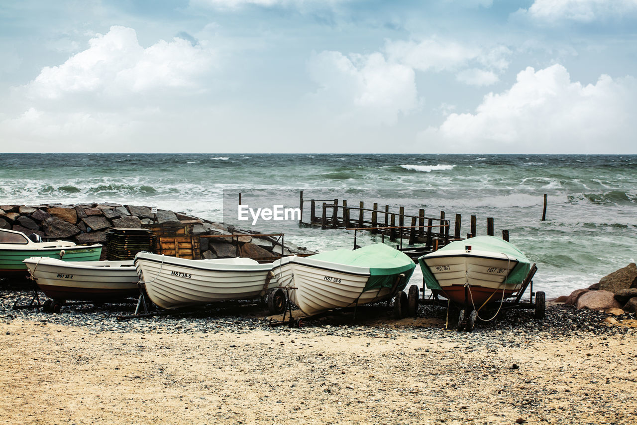 Boats moored on shore at beach against sky