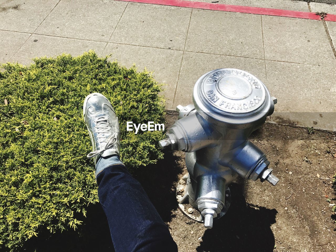 Low section of person wearing silver shoe by fire hydrant at sidewalk