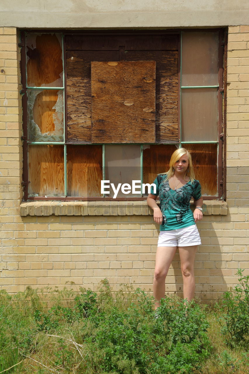 Portrait of girl standing against old abandoned building in grassy field