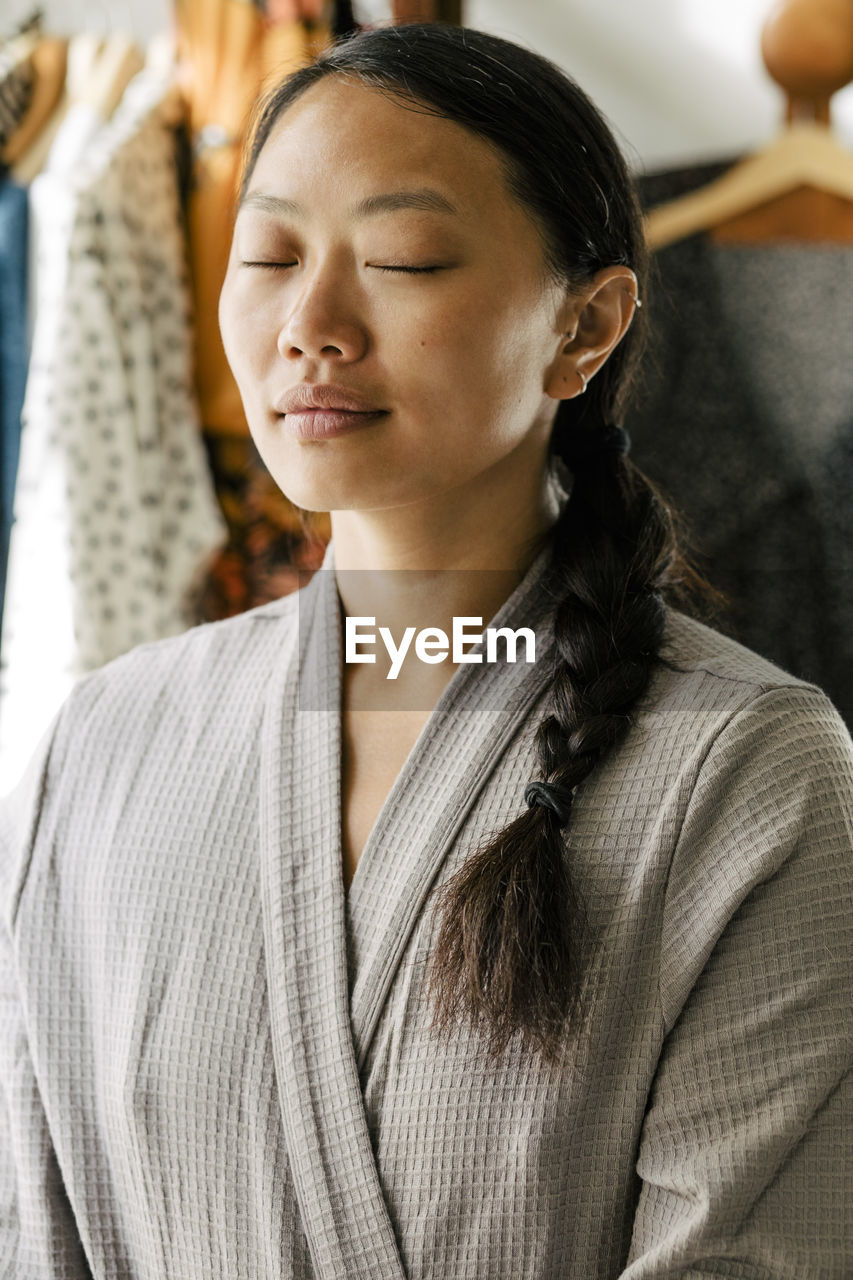 Young woman in bathrobe meditating at home