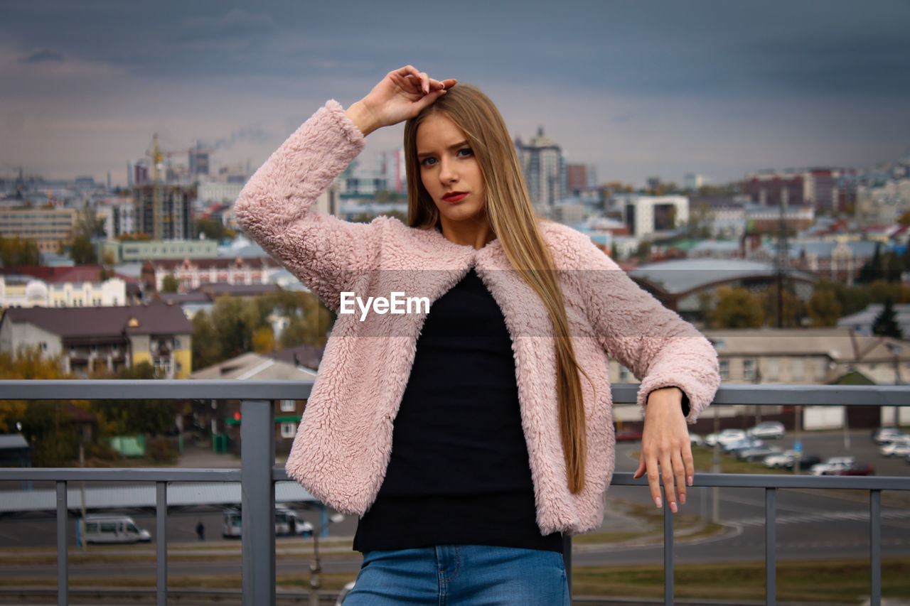 Portrait of young woman standing against cityscape in city