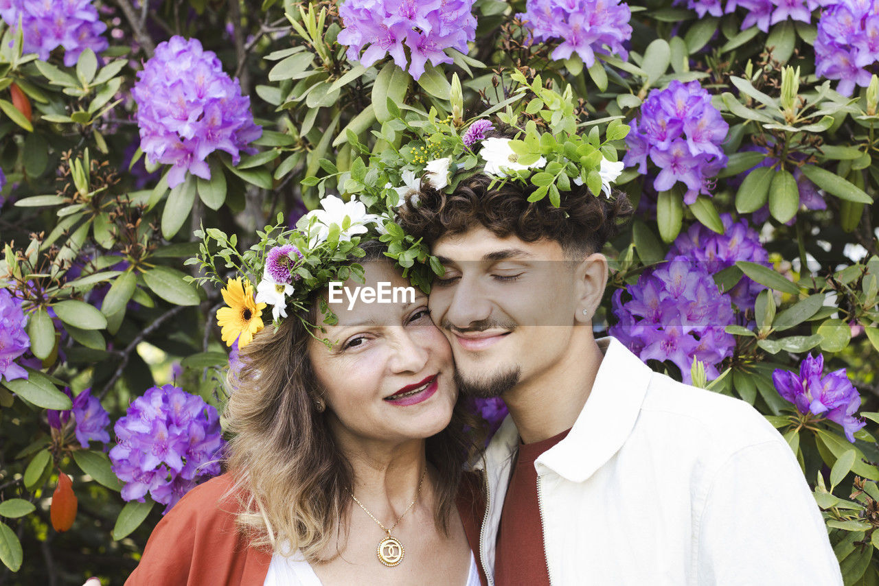 Smiling mother and son wearing tiaras against flower plants at back yard during swedish summer solstice