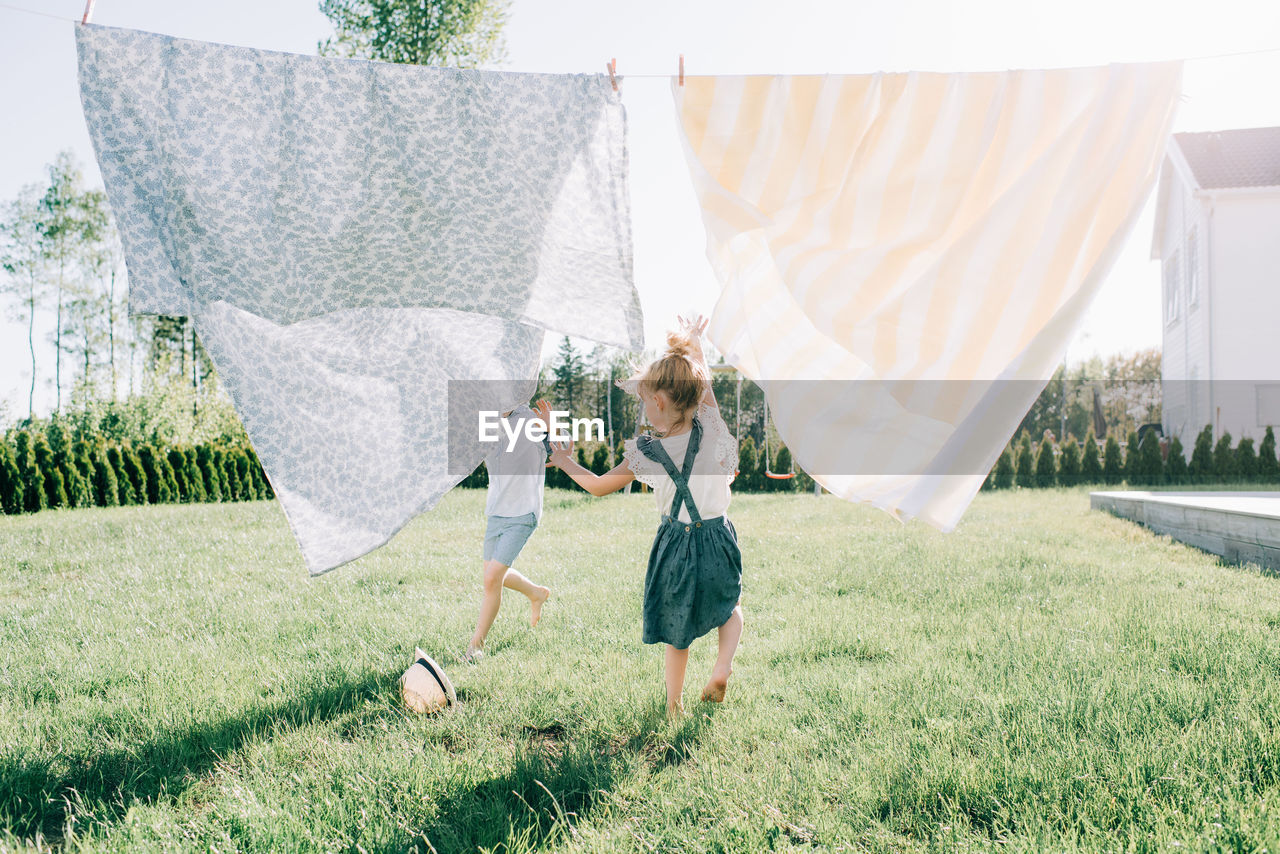 Siblings running through washing in the yard joyfully in summer