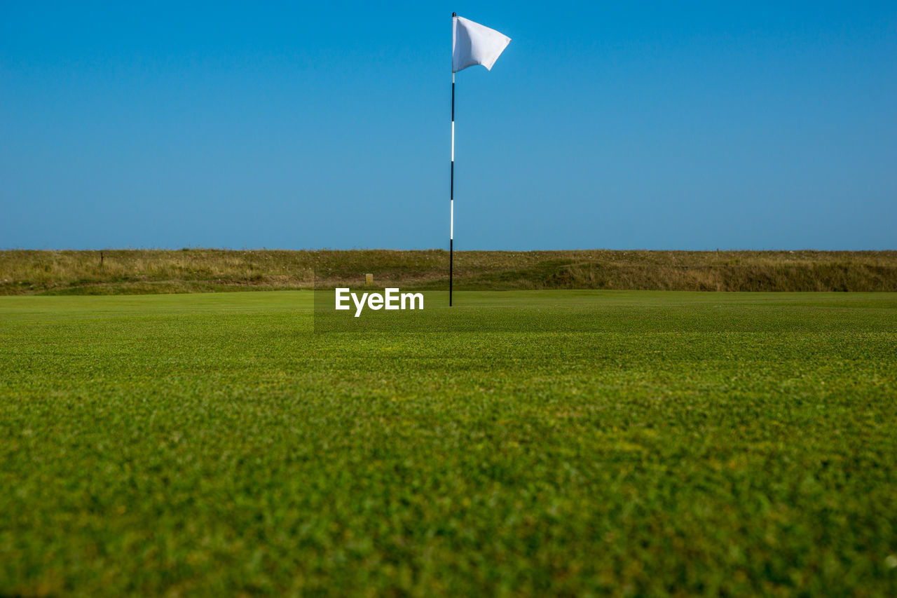 Golf flag on grassy field against clear blue sky