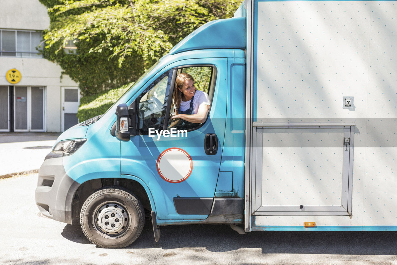 Confident young female owner driving food truck seen through window