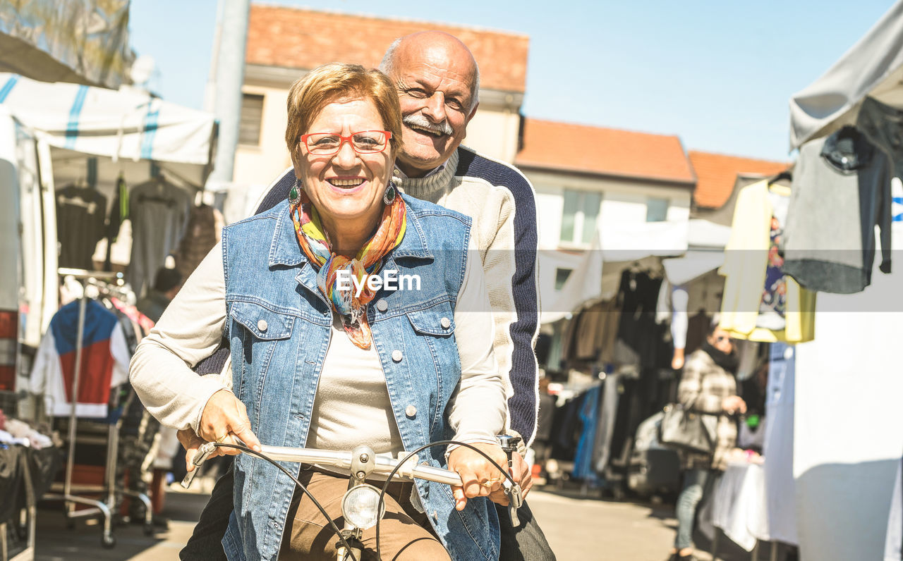 Portrait of smiling couple riding bicycle on road in city