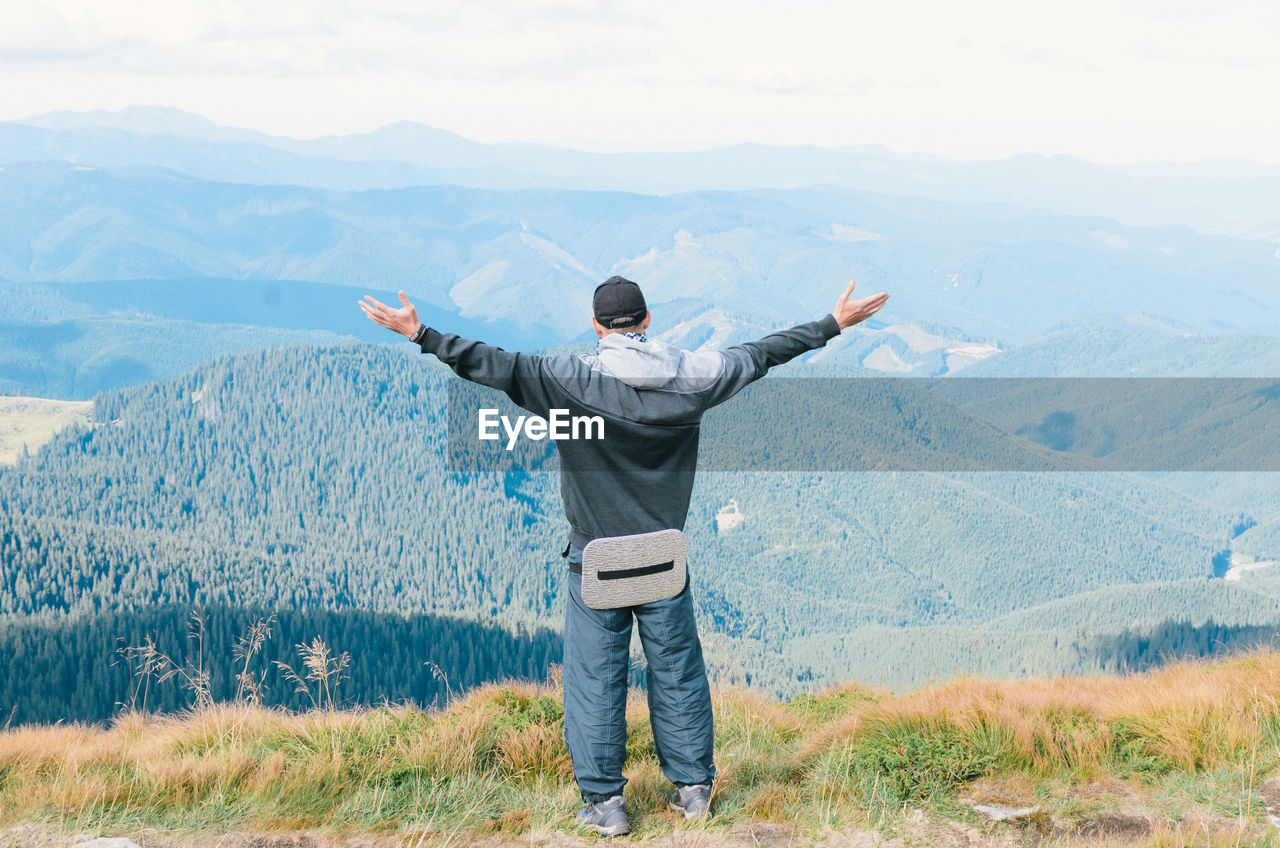 Rear view of hiker with arms outstretched standing on mountain