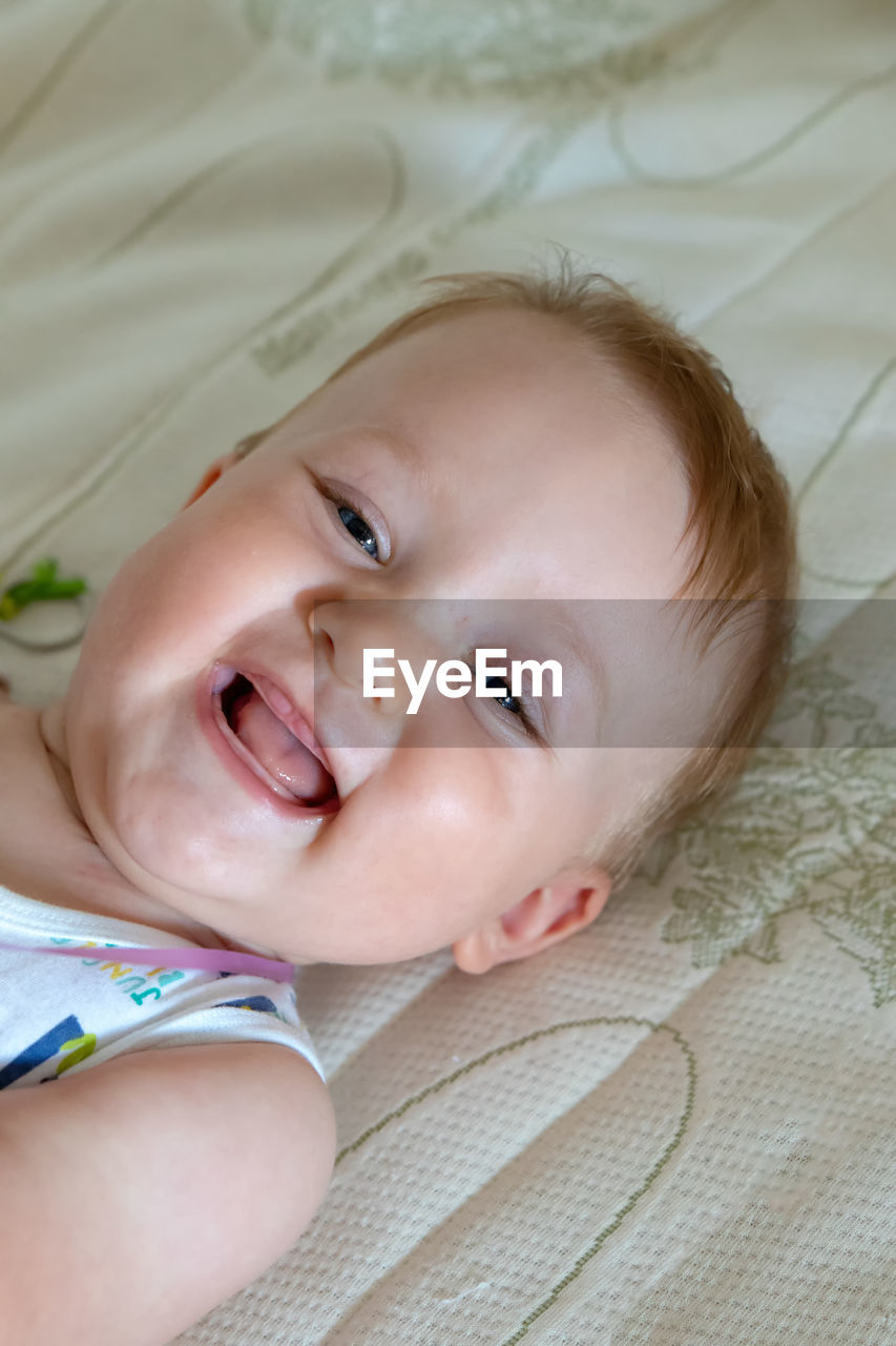 High angle portrait of baby boy smiling while lying on bed at home