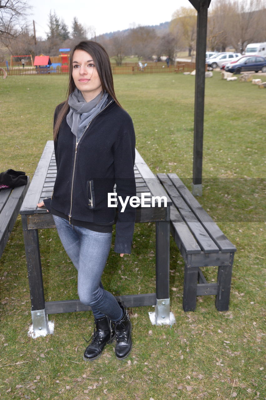 Smiling young woman standing by bench at park