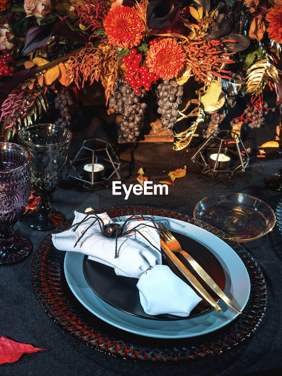 Table served in black halloween style. bouquet with red flowers, decorative spiders, pumpkins.