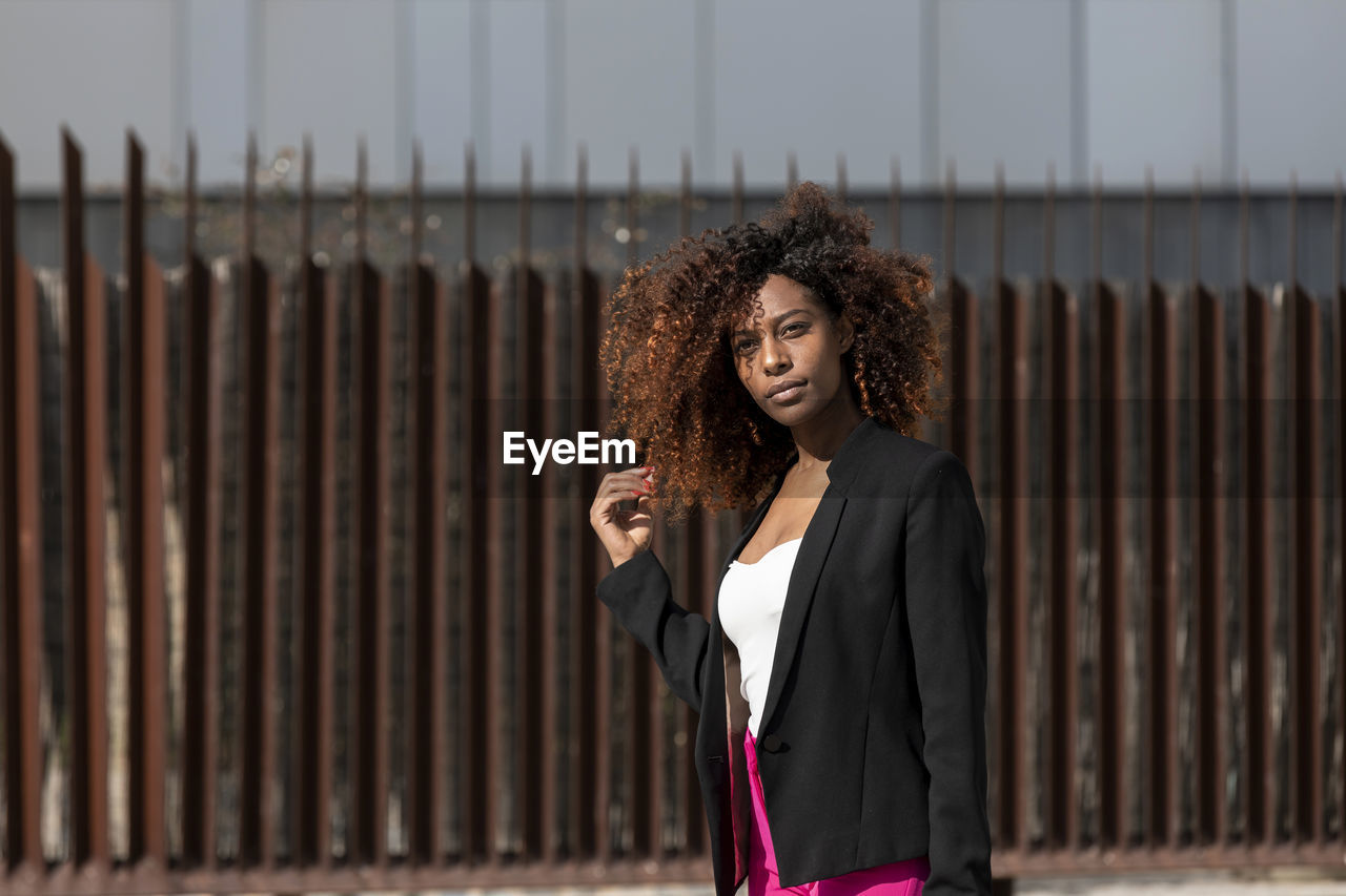 Young woman with curly hair standing against wall