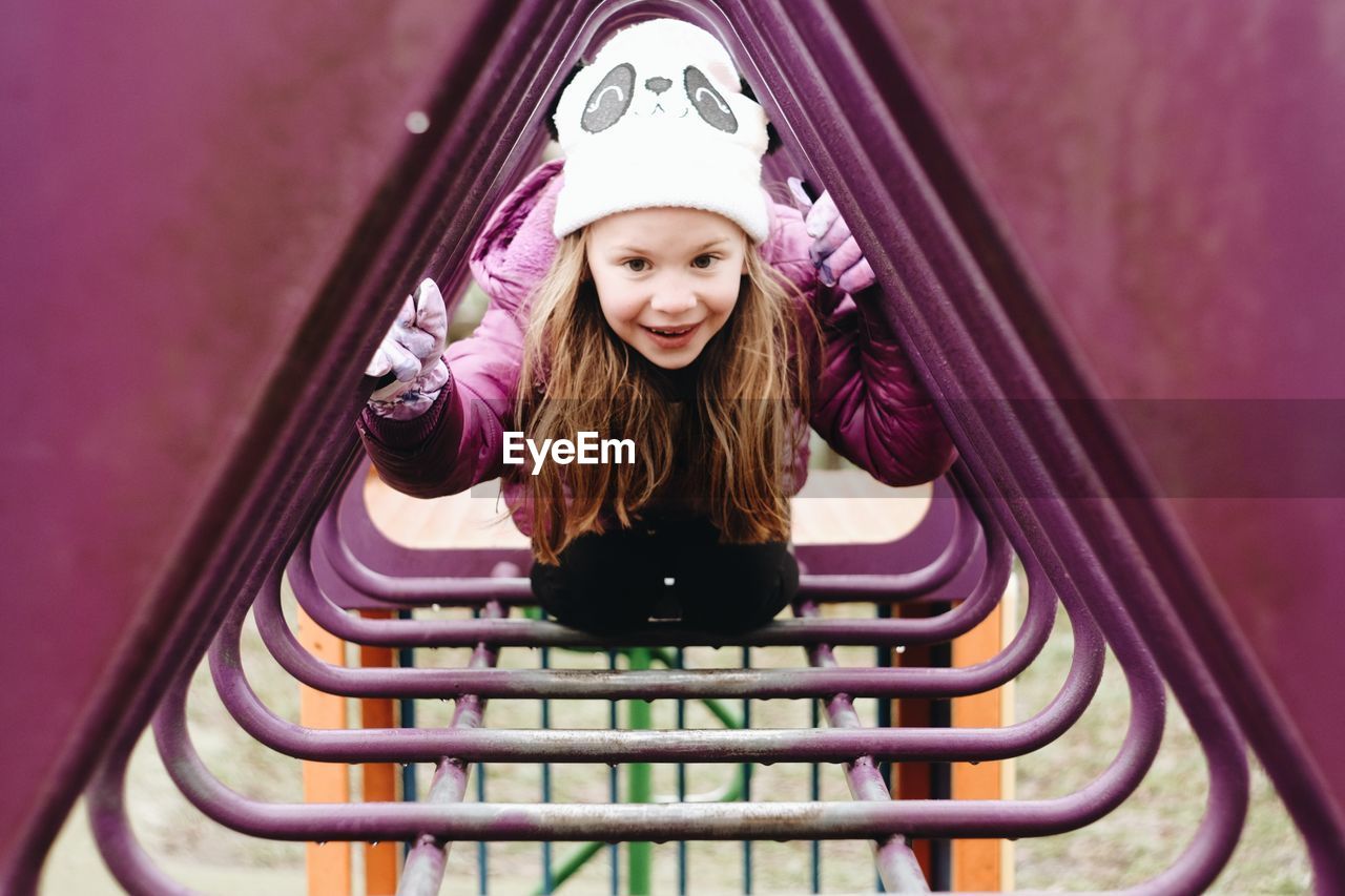 Smiling girl climbing through frame in playground