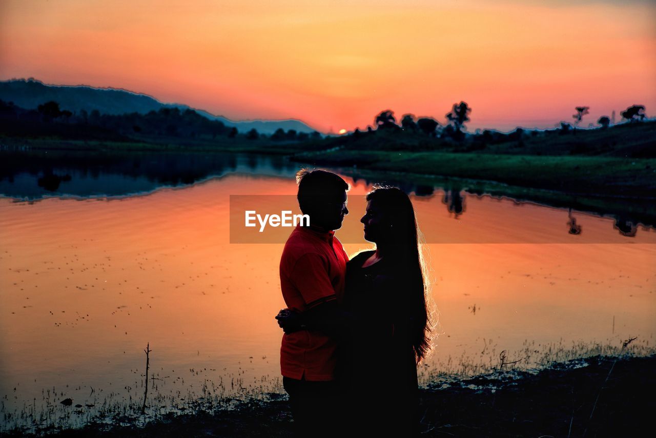 Couple embracing at lakeshore during sunset