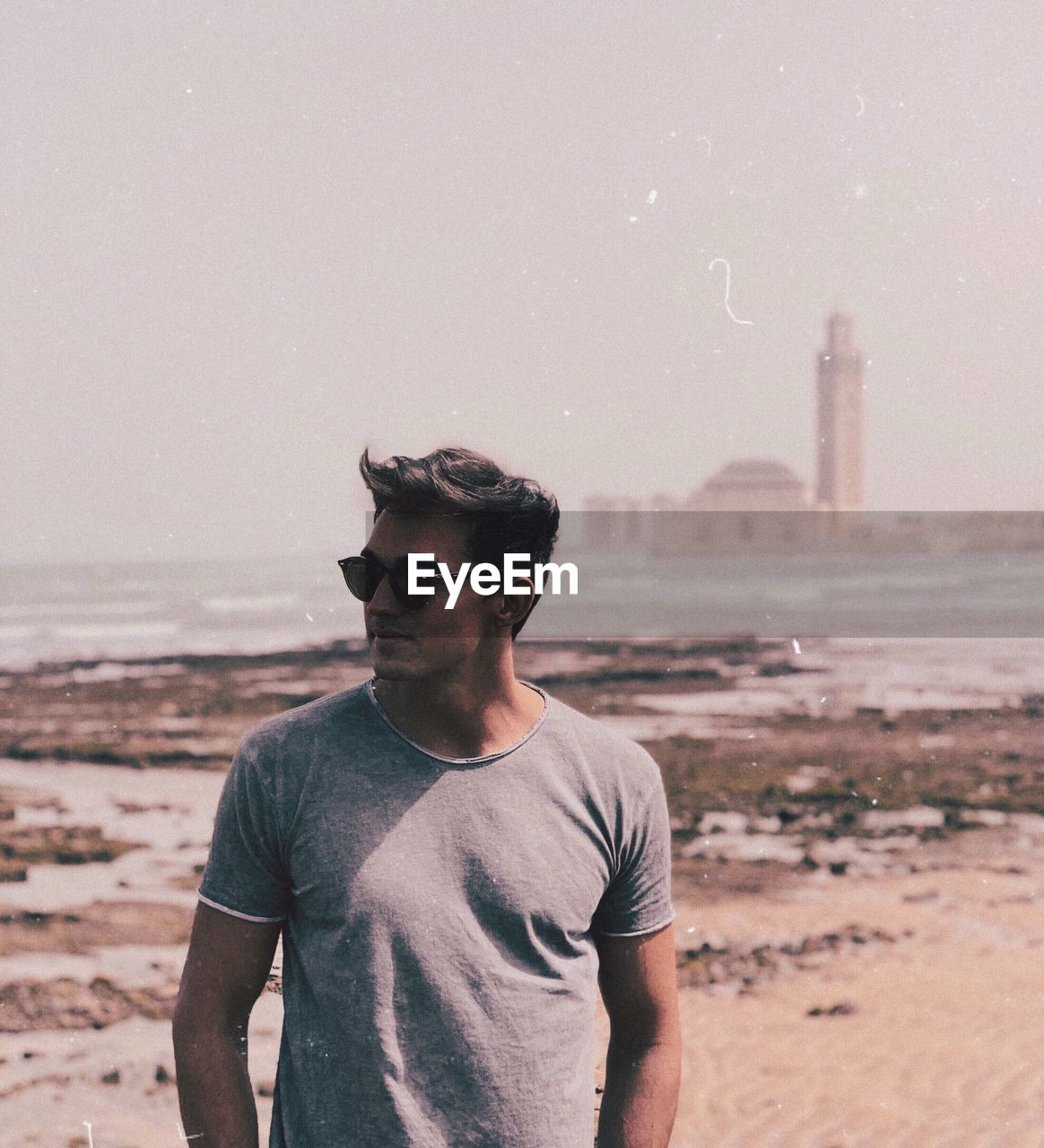 YOUNG MAN WEARING SUNGLASSES STANDING ON SHORE