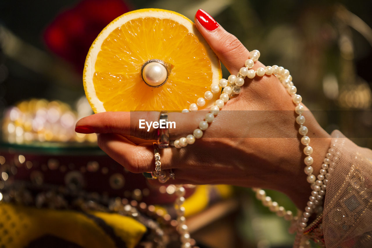 Cropped hand of woman wearing jewelry holding orange