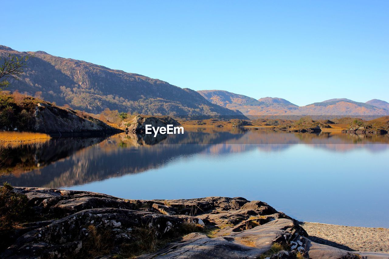 Scenic view of lake by mountains against clear blue sky