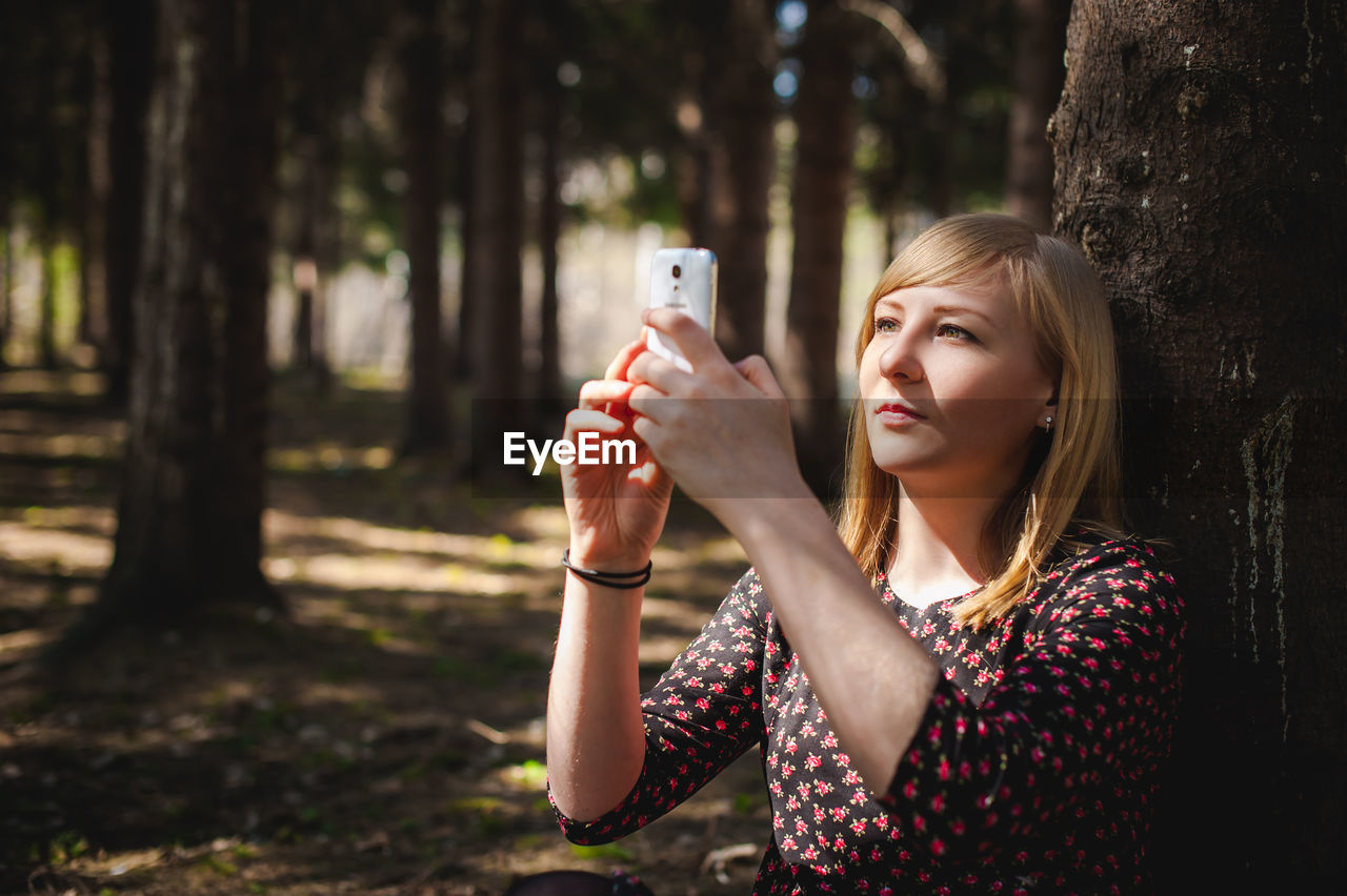 Woman using mobile phone by tree trunk in forest