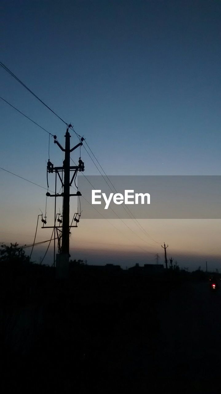 Low angle view of electricity pylon against sky at dusk