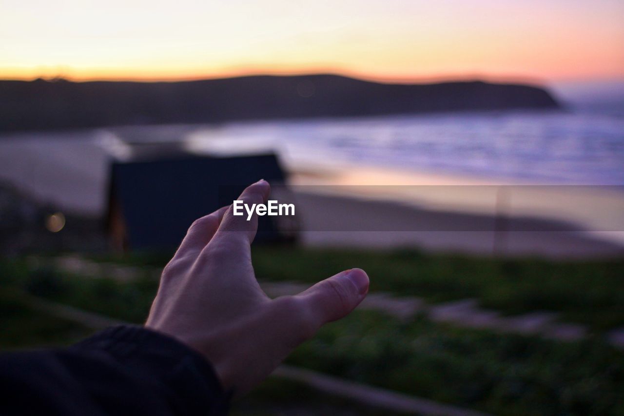 Cropped hand gesturing against beach during sunset