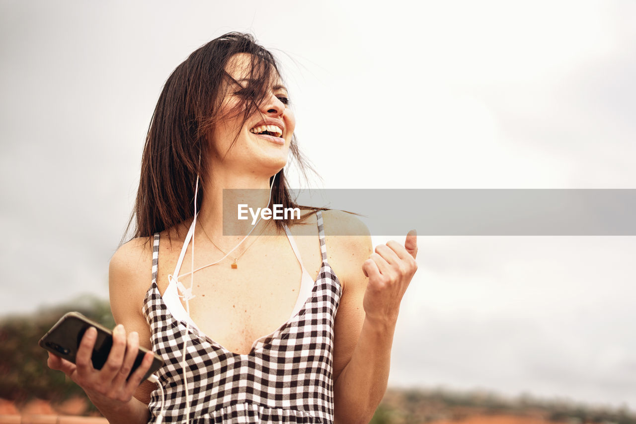 Happy woman listening music against sky
