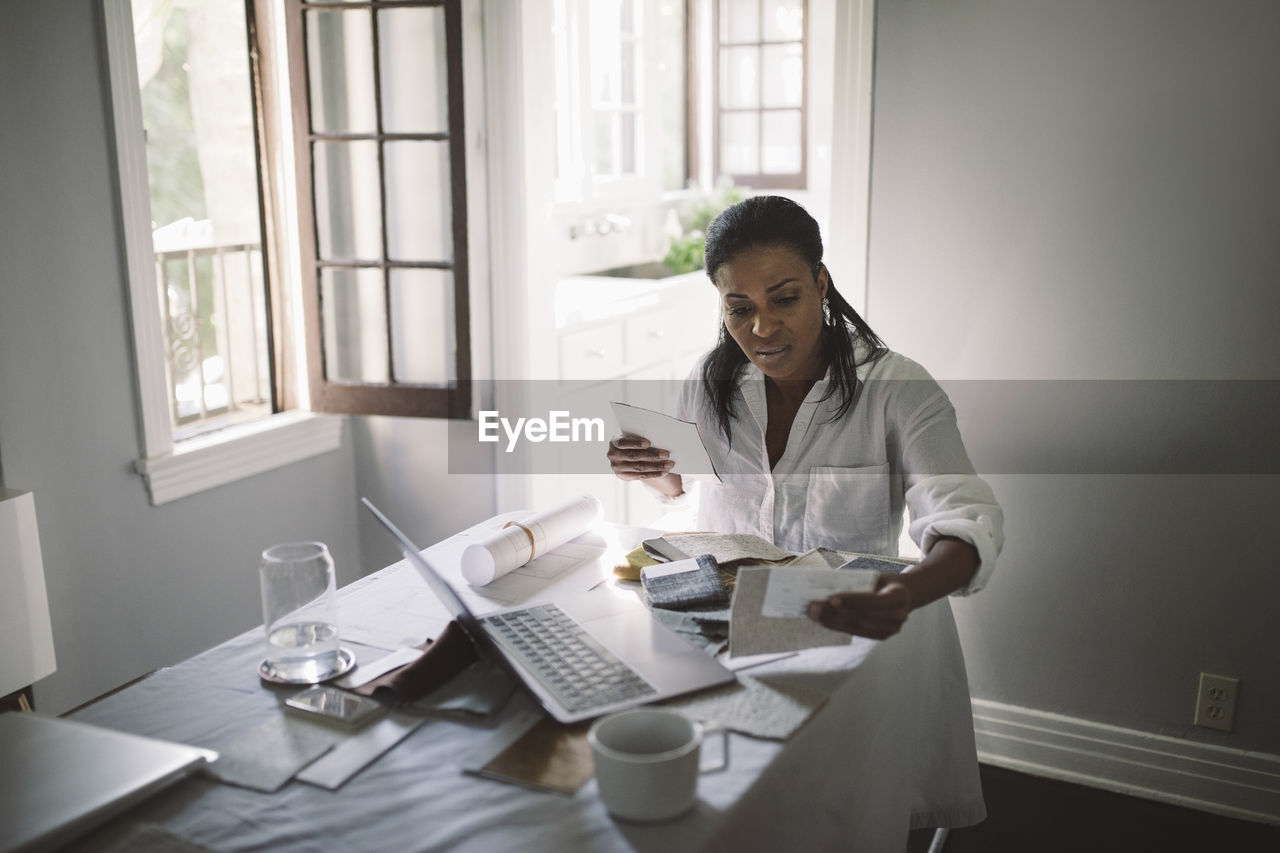 Female entrepreneur working while sitting by dining table at home office