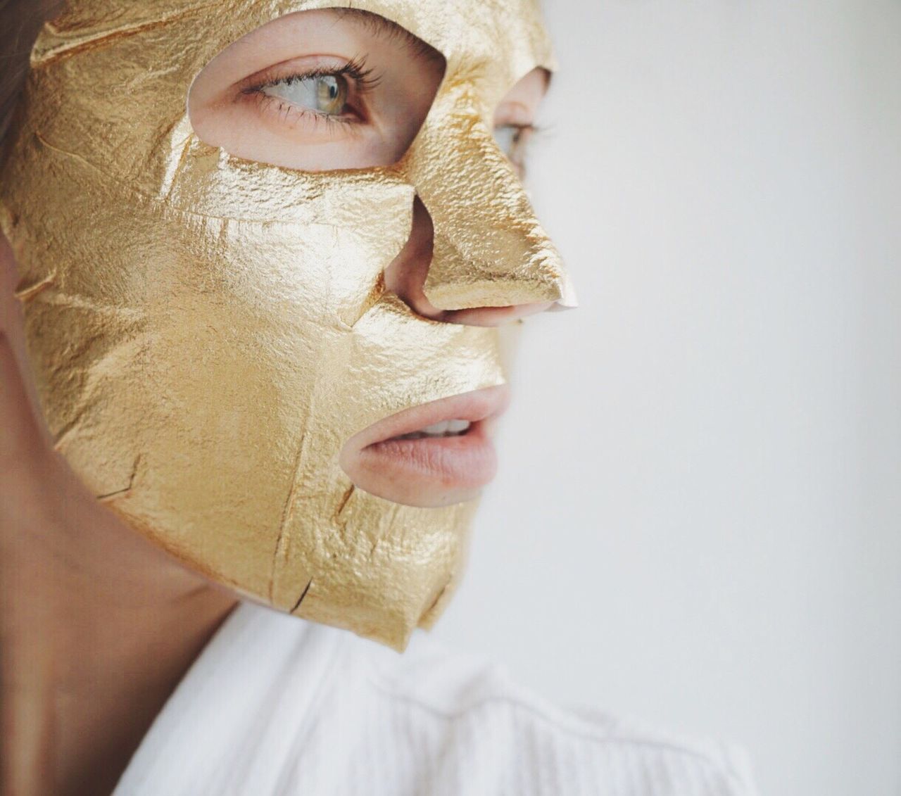 Close-up of woman with golden facial mask over white background