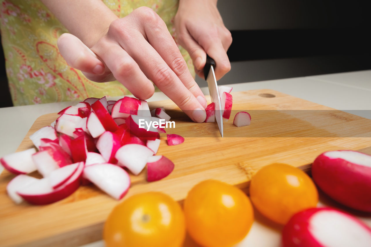 Close-up female hands of a young girl cut a fresh radish with a kitchen knife. preparing vegetable