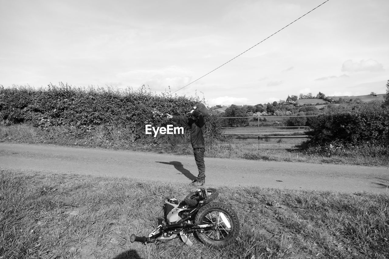 Side view of boy gesturing while standing on road against sky