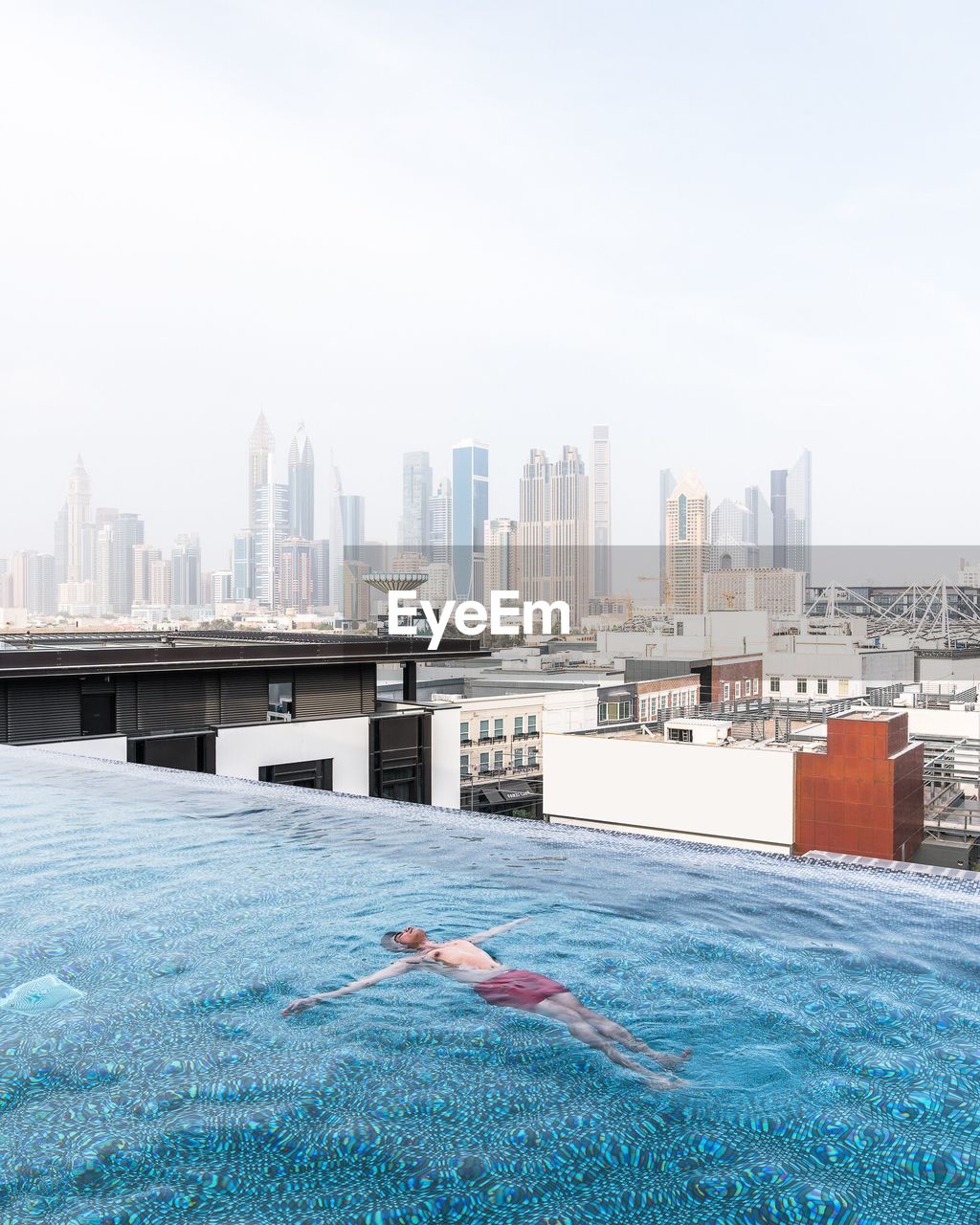 Shirtless man swimming in pool against cityscape