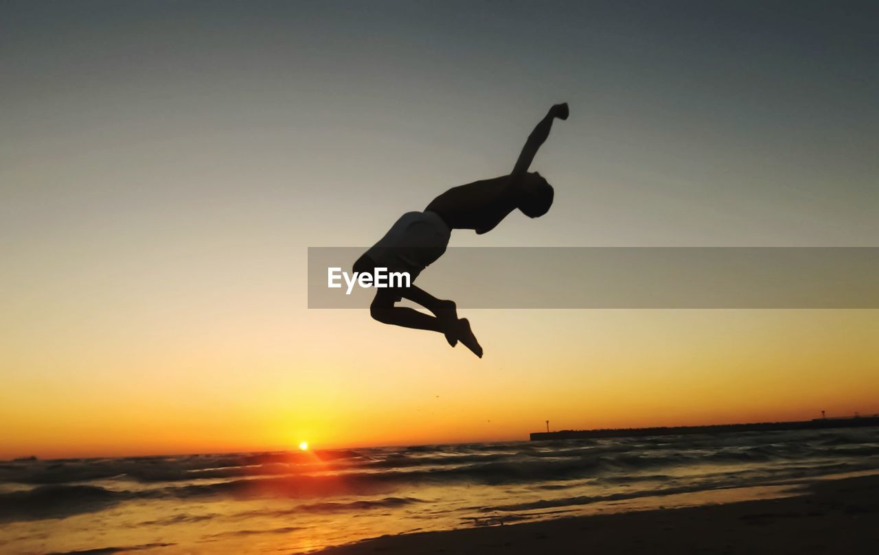 Silhouette man jumping at beach against sky during sunset