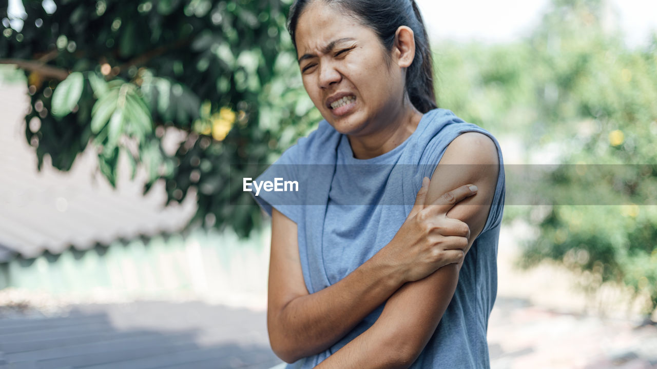 Woman touching shoulder in pain against trees