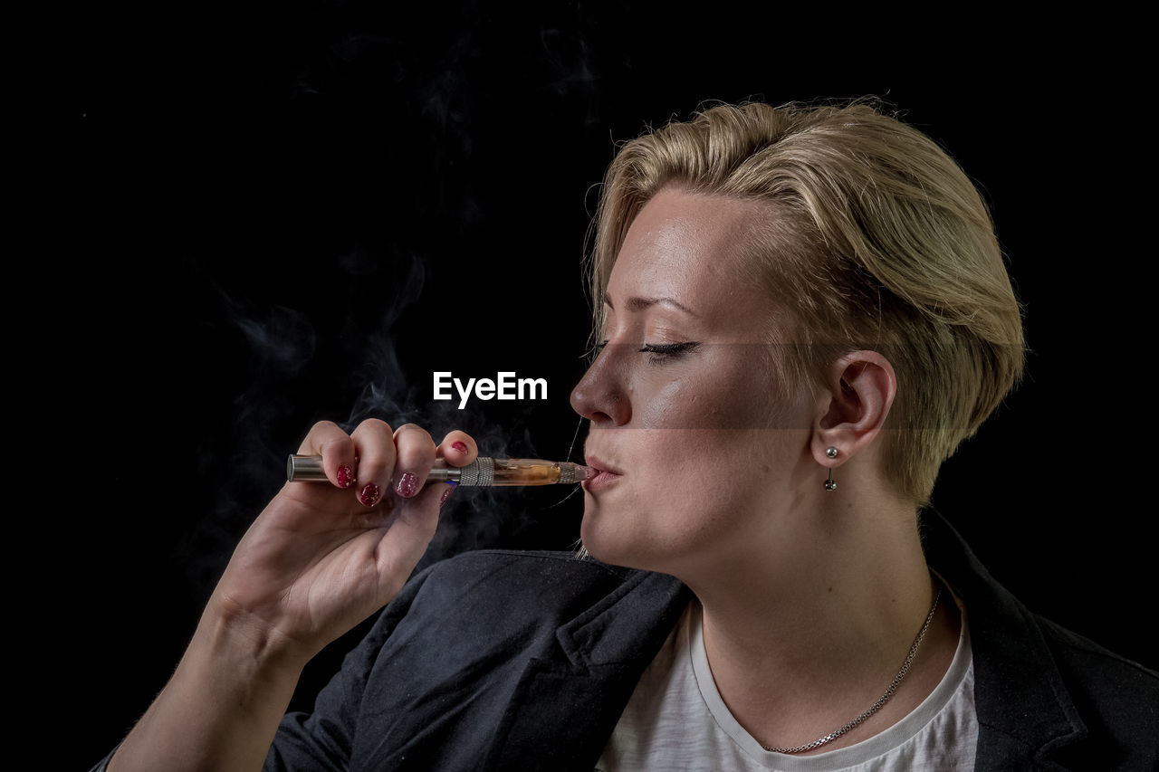 CLOSE-UP OF YOUNG MAN SMOKING AGAINST BLACK BACKGROUND