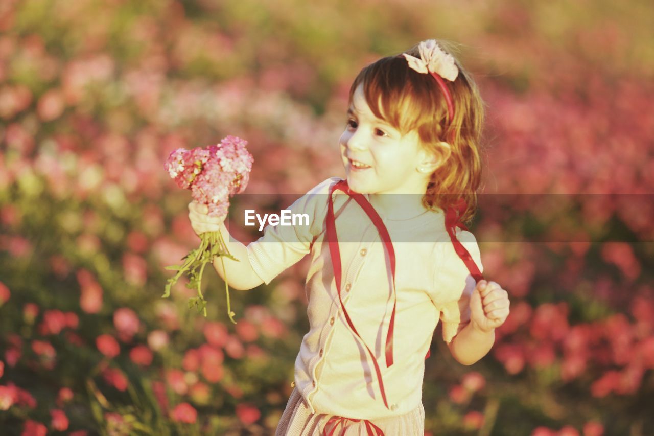FULL LENGTH OF GIRL STANDING BY FLOWERING PLANT