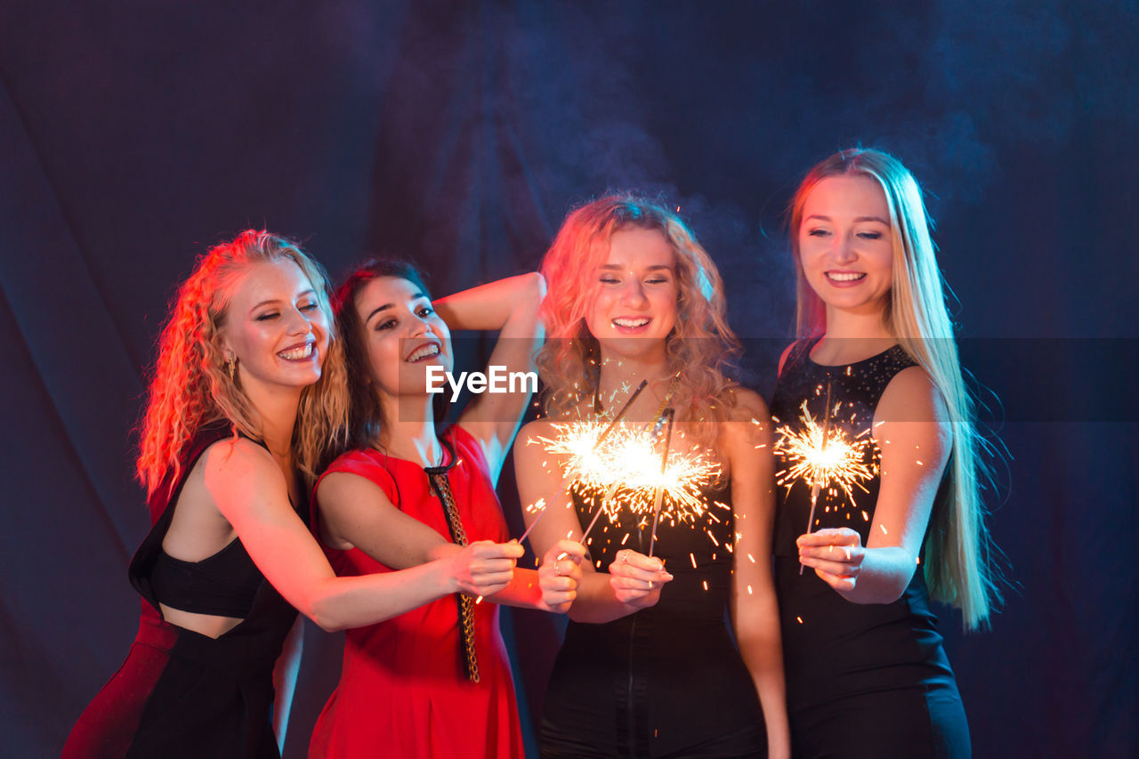 HAPPY YOUNG WOMAN STANDING IN FRONT OF ILLUMINATED LIGHTING EQUIPMENT