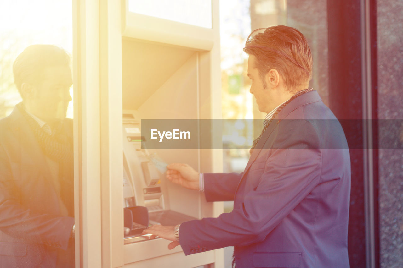 Side view of man using atm machine