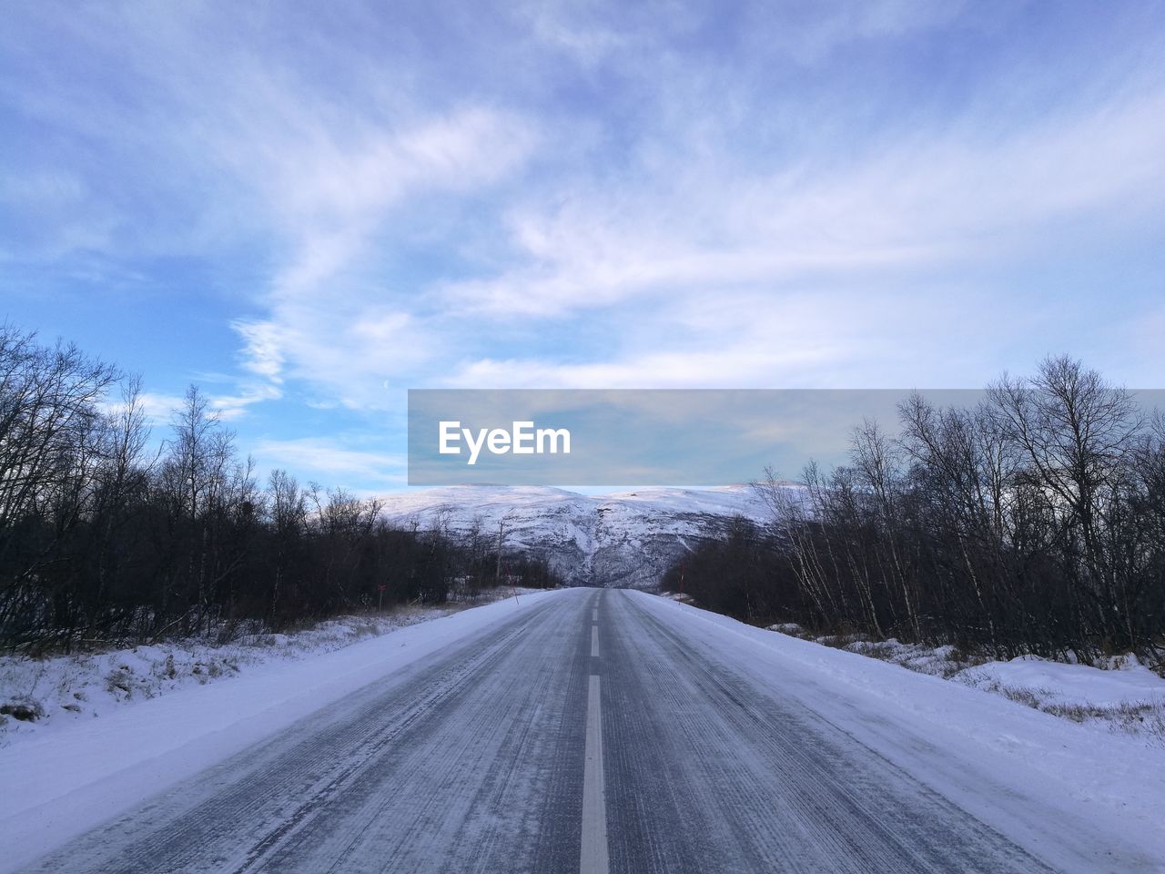 Road amidst snow covered landscape against sky
