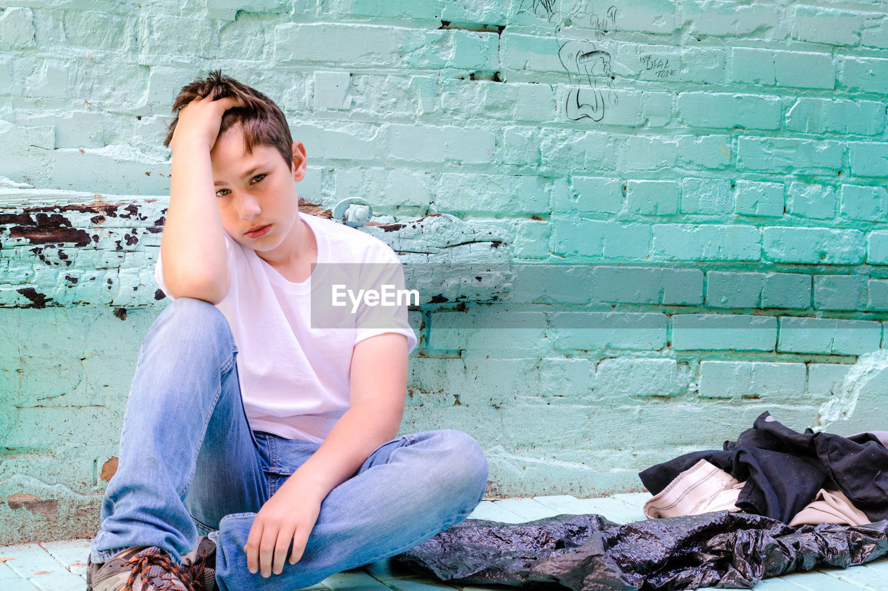 Full length of teenage boy sitting against wall