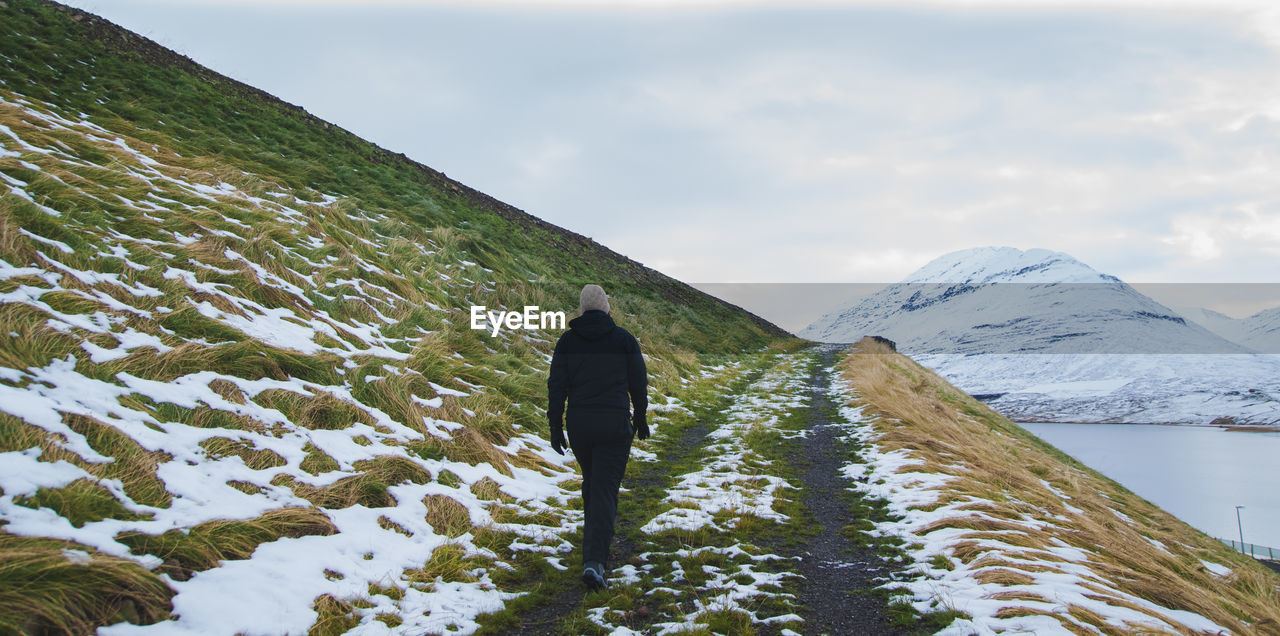 Rear view of woman walking on footpath against mountains and sky