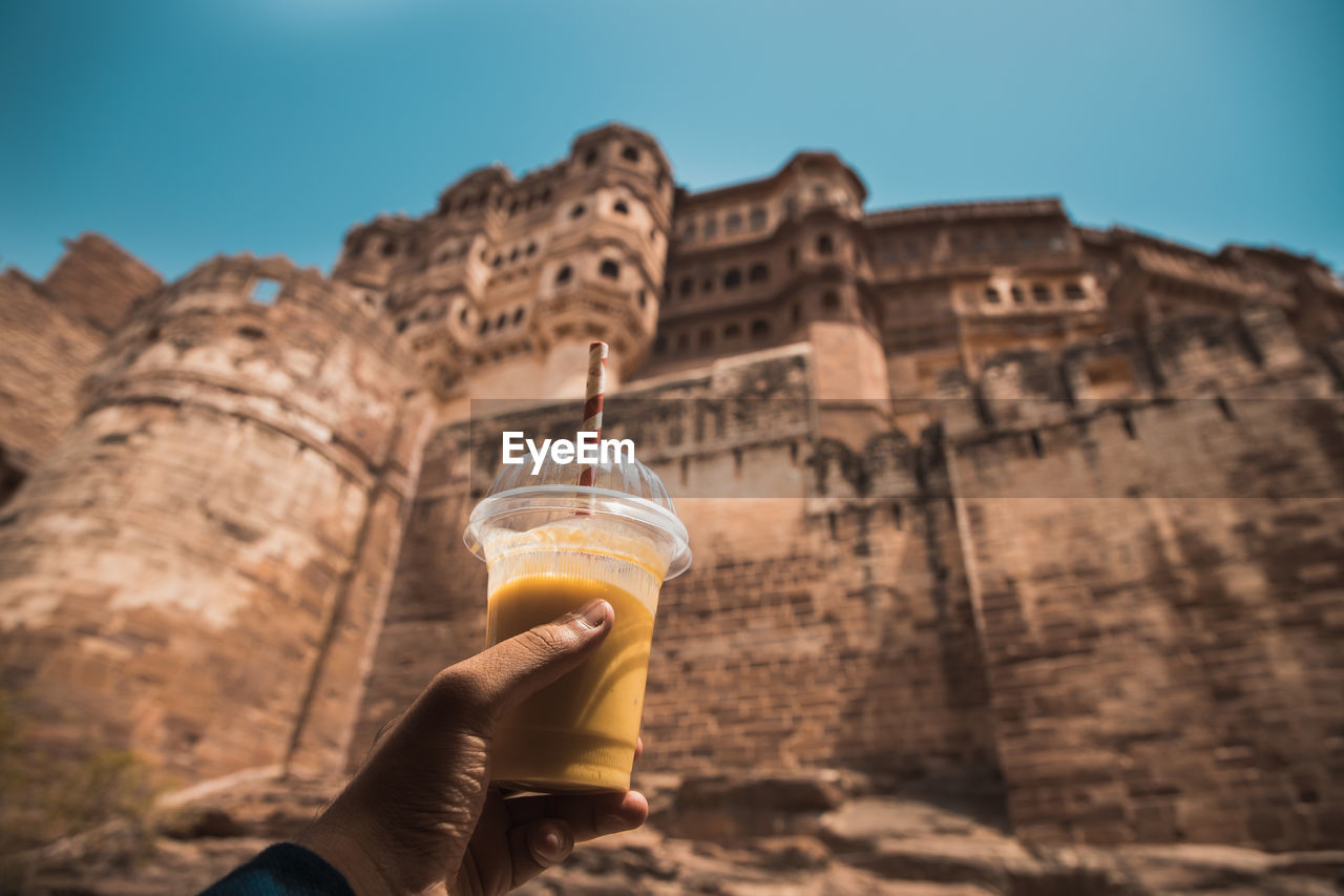 Midsection of person holding drink in a hot summer against a built structure of a fort