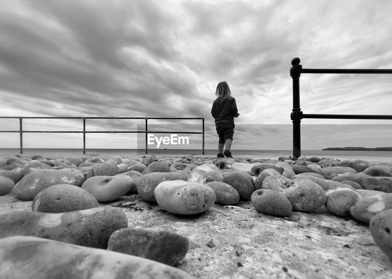 Rear view of child standing on rocks by sea against sky